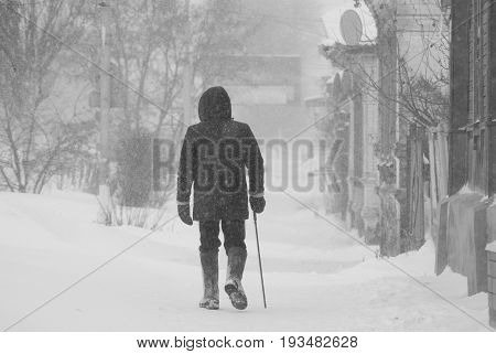 Lonely elderly man with a cane walking leisurely through a snow storm through the streets of the city.
