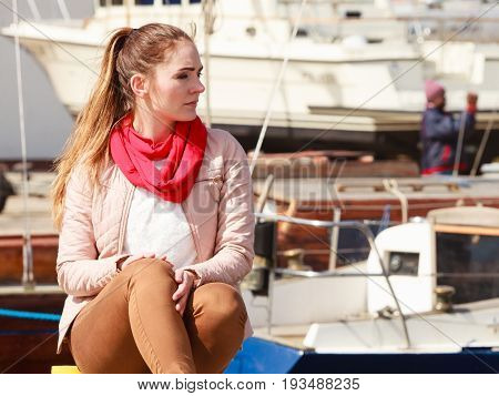 Woman sitting on bitt in marina waiting for somebody. Spring sunny weather outdoor shot.