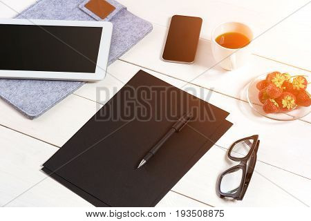 Modern workplace with digital tablet computer and mobile phone, cup of coffee, pen and empty sheet of paper. Top view and copy space for text. sun flare