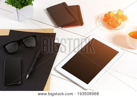Modern workplace with digital tablet computer and mobile phone, cup of coffee, pen and empty sheet of paper. Top view and copy space for text. sun flare