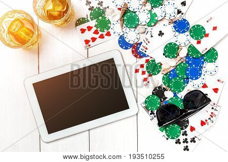 Gambling. Poker chips, cards and the dice nearby tablet on white wooden table. Top view. Copyspace. Poker. Summer. Sun flare