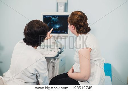 Doctor showing baby ultrasound image on computer to pregnant woman.