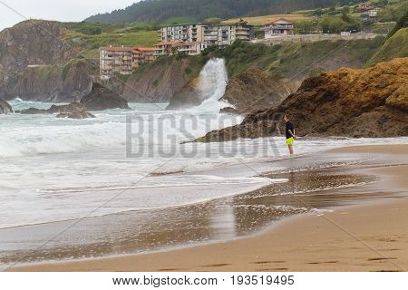 BAKIO SPAIN - JULY 4 2016: Unknown tourists on a beach. The young man costs on the beach and observes a storm
