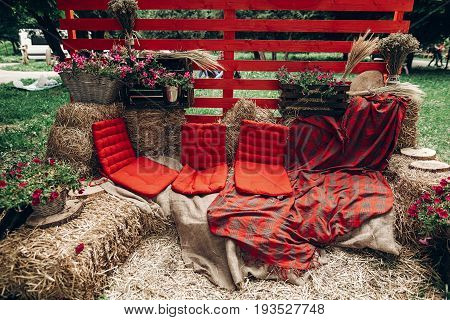 rustic photo booth. rural photo zone with haycocks hay chairs and flowers arrangement at wedding reception in summer park. street food festival