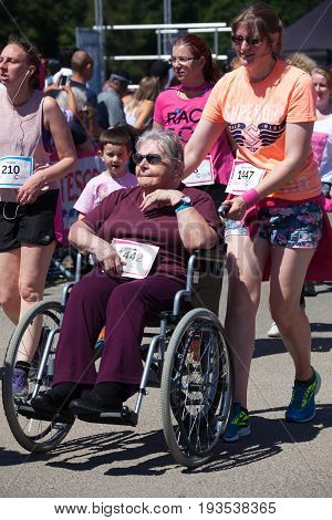 SOUTHAMPTON UK - July 2 2017: Race for Life women run and walk to raise money for Cancer Research charity in Southampton UK.Woman in a wheelchair bing pushed in wheelchair during race.