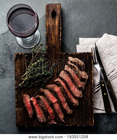 Slices of beef medium rare steak on wooden board, glass of red wine on slate background