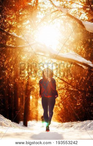 Young beautiful redhead sport woman running through the winter forest at sunset