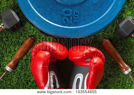 Dumbbells skipping rope boxing gloves and weight on green artificial grass