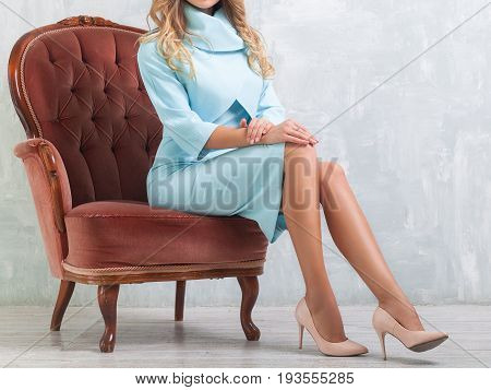 Young slender fashionable woman in a beautiful blue dress sitting on the a expensive classic brown armchair