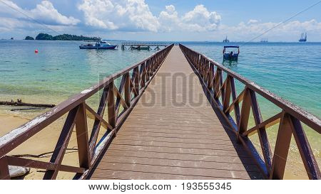 Wooden jetty over the beautiful Rusukan Besar island tropical beach with blue sky and clouds in Labuan Pearl of Borneo,Malaysia.