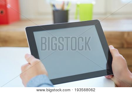 Man's hands holding tablet computer closeup on a light wooden table. Concept man working in the morning from home using tablet computer.
