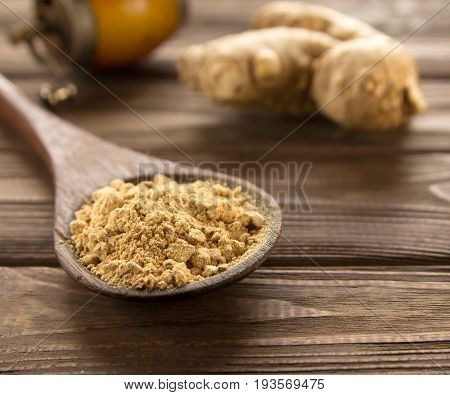 Spice ginger powder in a wooden spoon on a dark wooden background a vintage hand mill and ginger root. Close-up.