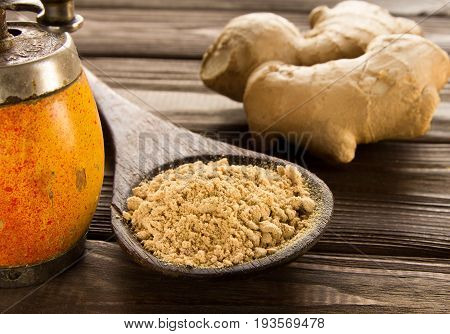 Spice ginger powder in a wooden spoon on a dark wooden background a vintage hand mill and ginger root. Close-up.