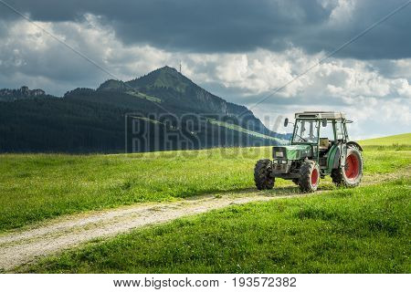 Old tractor on a meadow with fresh grass. Beautiful view to alpine mountains. Alps.