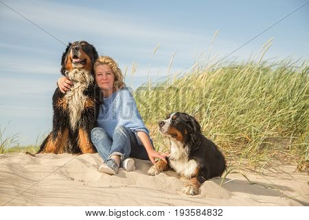 mature woman with her dogs on sand and grass sitting