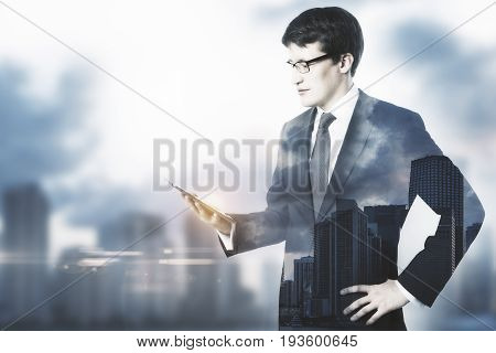 Attractive young businessman using cellphone on blurry city background with copy space. Social media concept. Double exposure