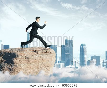 Side view of young businessman jumping off cliff on city background. Hope concept