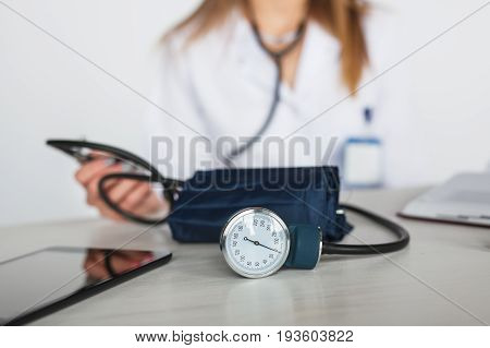 Anonymous woman in medical uniform sitting at table with pulsometer and tablet.