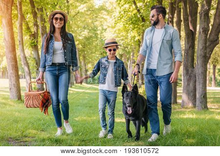 Young Happy Interracial Family With Picnic Basket Walking With Dog In Forest