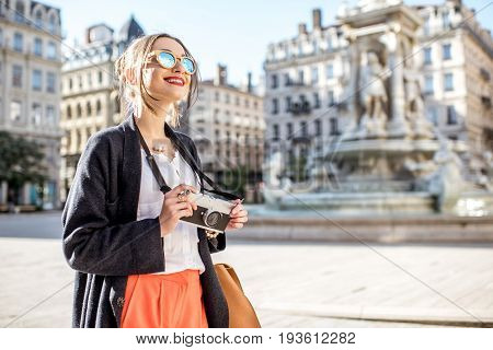 Young woman standing with photo camera on the Jacobins square with famous fountain on the background in Lyon city in France