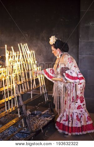 El Rocio Spain - June 2 2017: Female pilgrim in traditional spanish dress lights up candles in the hermitage of El Rocio during the Romeria 2017. Andalusia Spain