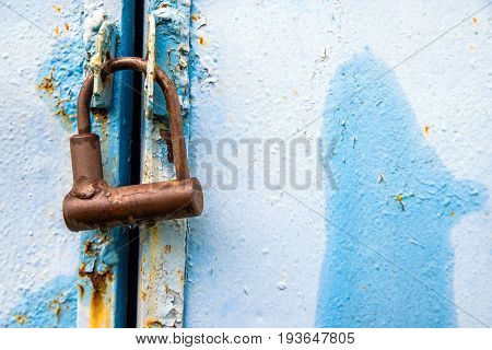 Rusty padlock hanging on a blue metallic background
