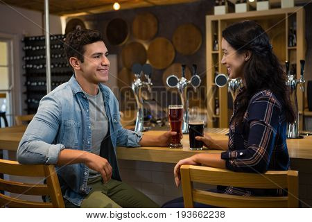 Smiling friends enjoying drinks while sitting on chairs at bar