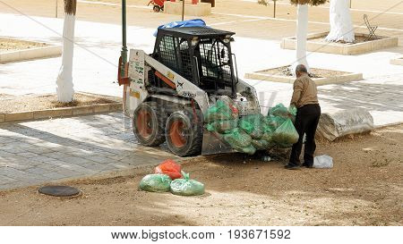 Jerusalem, Israel - May 21, 2017: Street sweeper senior man takes garbage bags and puts it in cleaning sweeper vehicle. Jerusalem municipality employs arab workers to clean the city streets.