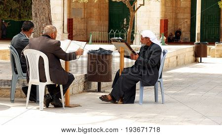 Jerusalem, Israel - May 21, 2017: Three senior Muslims pray and read the Quran at the entrance of Al-Aqsa mosque in Jerusalem or Quddus. Al Aqsa mosque is a sacred place for all muslims and islamic