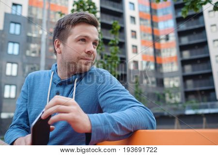 Portrait of mature man in casual clothing using digital tablet outdoors. Youngman sitting in city yard looking at his digital tab for directions and location.