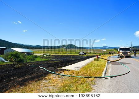 KALISPELL, MONTANA, USA - June 21, 2017: Firefighter rolling up hose in the front yard of a home threatened by a contained grass fire