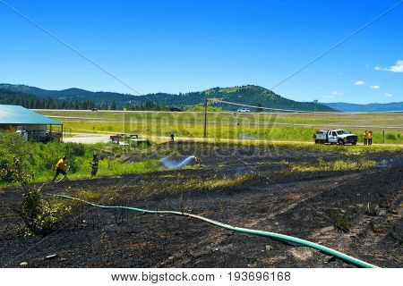 KALISPELL, MONTANA, USA - June 21, 2017: Firefighter rolling up hose in the front yard of a home threatened by a contained grass fire