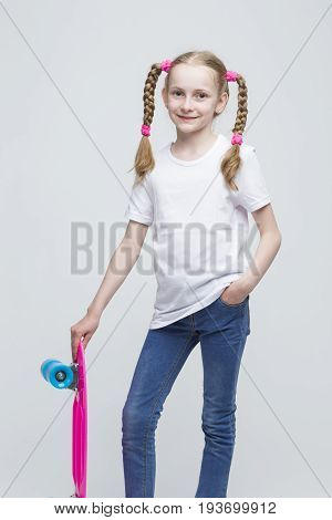 Kids Concepts. Portrait of Little Caucasian Blond Girl with Nice Pigtails Posing With Pink Pennyboard Against White Background. Vertical Image