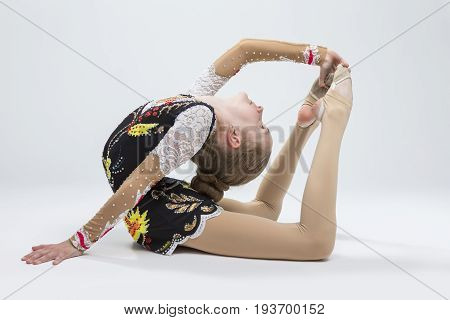 Sport Ideas. Young Caucasian Female Rhythmic Gymnast Athlete In Professional Competitive Suit Doing Backbend Stretching Exercise Pose in Studio Against White.Horizontal Image