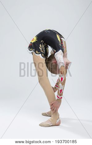 Sport concepts and Ideas. Young Caucasian Female Rhythmic Gymnast Athlete In Professional Competitive Suit Doing Backbend Stretching Exercise While Posing in Studio Against White. Vertical Shot