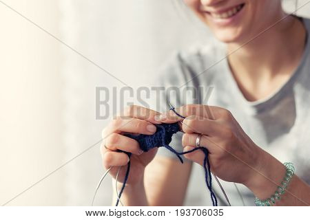 A young woman knits with a knitting sweater of natural wool. Smiling close-up