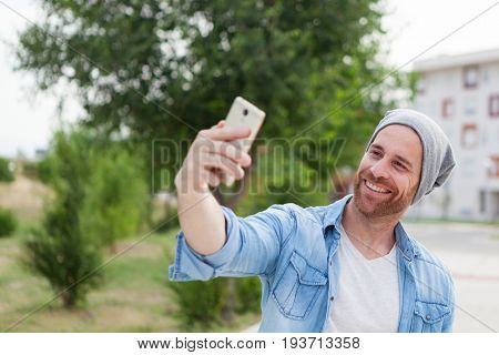 Casual fashion guy taking a photo himself with a mobile in the city