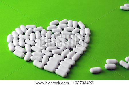 White Heart Made Of Pills On A Green Background.