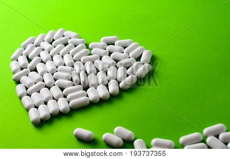 White Heart Made Of Pills On A Green Background.