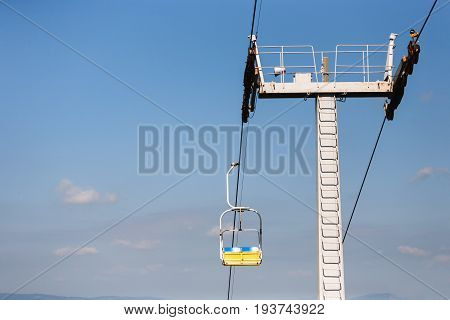 Mountain lift. Ropeway construction against blue clear sky. Yellow cabin moving on cableway, background