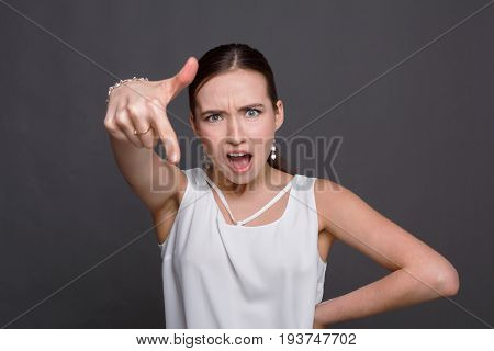 Young woman in white shirt specifies with finger to down. Pretty girl shout and point under, advertisement background
