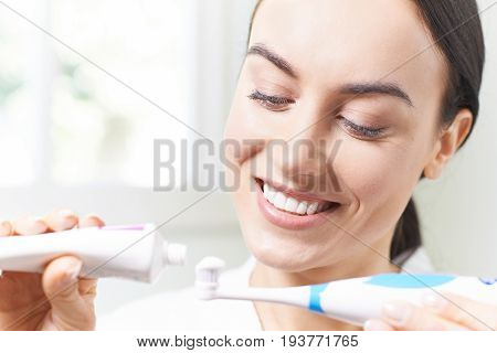 Woman Squeezing Toothpaste Onto Electric Toothbrush In Bathroom