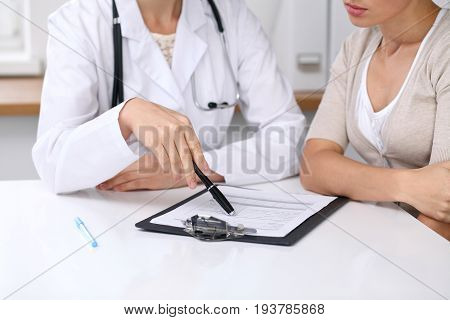 Close up of doctor and patient sitting at the desk while physician pointing into medical form hystory. Medicine and health care concept.