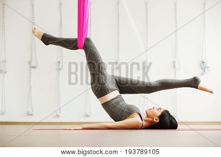 Aerial yoga exercise or antigravity yoga, woman stretching one leg, other fixed in hammock in sport studio or gym. Teenage girl building strength, enhancing flexibility, easing sore joints or muscles