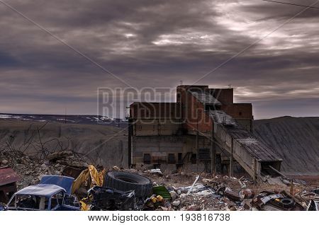 Old abandoned back in the middle of a huge garbage dump of various metal scraps and boards against the background of a stormy sky