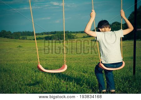 Sad lonely boy sitting on swing. Back view
