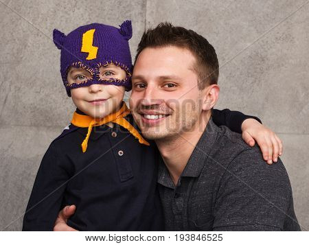 Charming kid wearing superhero hat and posing with father in studio.