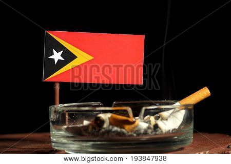 East Timorese Flag With Burning Cigarette In Ashtray Isolated On Black Background
