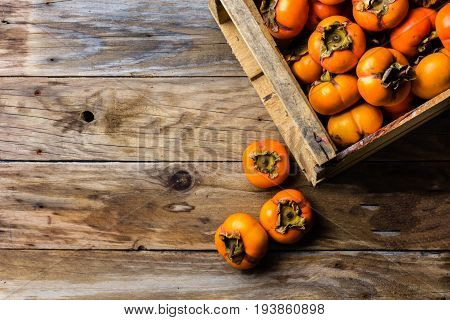 Box Of Fresh Fruits Persimmon Kaki On Wooden Background. Copy Space