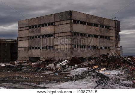 Old abandoned back in the middle of a huge garbage dump of various metal scraps and boards against the background of a stormy sky